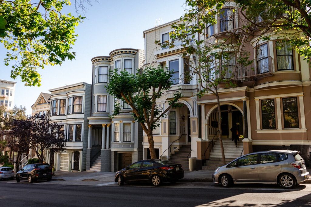 Charming Victorian houses on a sunny San Francisco street lined with trees and parked cars.