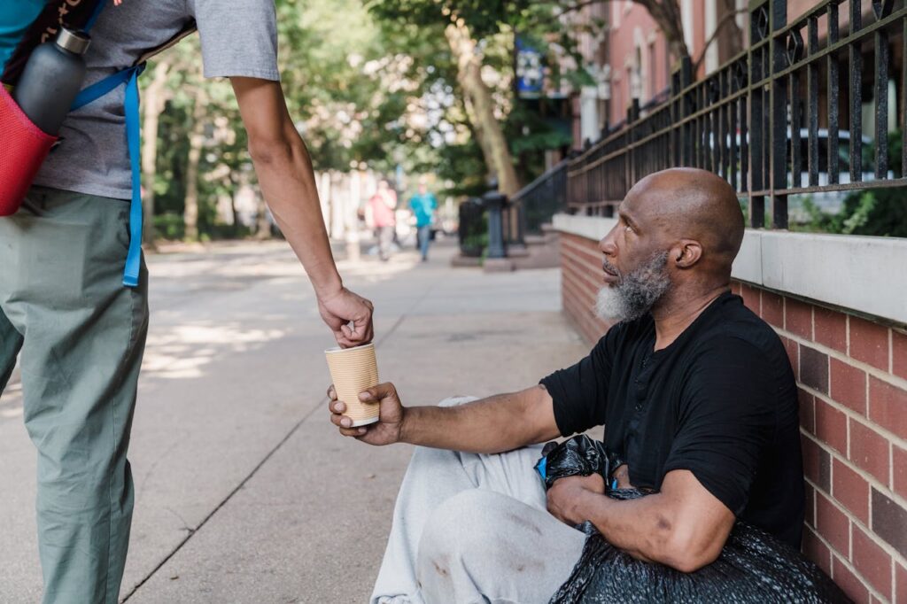 A person offers money to a homeless man sitting on the sidewalk, highlighting urban compassion.