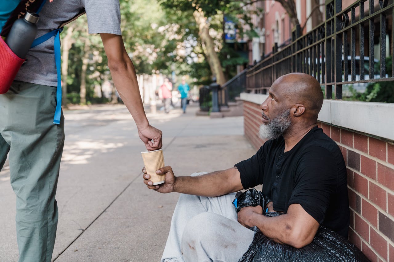 A person offers money to a homeless man sitting on the sidewalk, highlighting urban compassion.